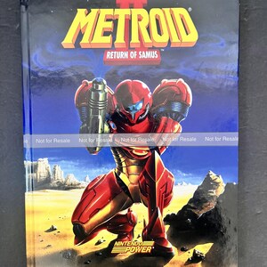 May include: A hardcover book titled Metroid II Return of Samus with a graphic illustration of a red and gold armored character kneeling on a desert landscape. The cover features the Nintendo Power logo and a repeating Not for Resale watermark.
