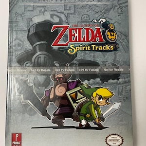 May include: A gray and silver book cover for the video game The Legend of Zelda: Spirit Tracks. The cover features a cartoon image of Link and a large, armored enemy. The book is a Prima Games guide and has the text "Premiere Edition" at the top.