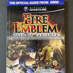 May include: A Fire Emblem: Path of Radiance official player's guide for the Nintendo GameCube. The cover features the game's title in fiery orange and yellow, with character illustrations. The guide is marked "Not for Resale."