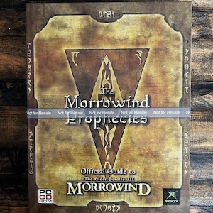 May include: A vintage copy of "The Morrowind Prophecies: Official Guide to The Elder Scrolls III" for PC and Xbox. The cover features a brown and gold design with the game's logo and a central emblem. The words "Not for Resale" are printed across the top.
