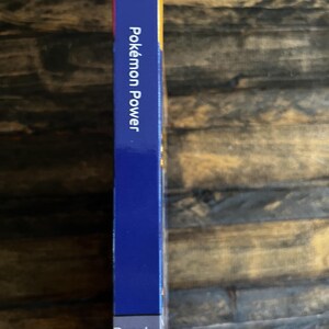 May include: A blue rectangular box with the text "Pok&eacute;mon Power" in white. The word "Resale" is printed in white at the bottom of the box. The box is on a wooden surface.