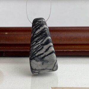 May include: A black and white striped stone pendant on a silver chain. The stone is a triangular shape with a smooth, polished surface.