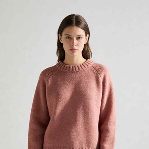 Può includere: Un maglione rosa polveroso con girocollo a coste e maniche lunghe. Il maglione presenta una maglia strutturata e un orlo a coste. La modella indossa pantaloni neri. Uno stile classico e confortevole.