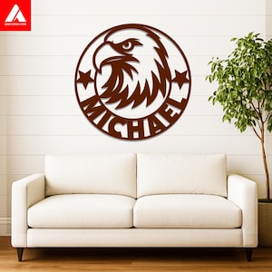 May include: A circular brown wall sign featuring a stylized eagle head profile at the top, two five-pointed stars on the sides, and the name MICHAEL in bold capital letters integrated into the lower portion of the circular frame design.