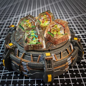 Puede incluir: Cuatro teclas de plástico transparente con escenas en miniatura en su interior. Cada tecla presenta un personaje diferente de las Tortugas Ninja en un escenario verde, marrón y amarillo. Las teclas se muestran en una base redonda de metal gris oscuro y dorado.