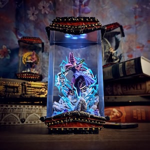 Puede incluir: Una detallada figura de un personaje en una vitrina de cristal. La figura está vestida de morado y azul, con un bastón y rodeada de energía azul. La vitrina tiene una base y una parte superior decorativas y ornamentadas, con una combinación de colores rojo y negro.