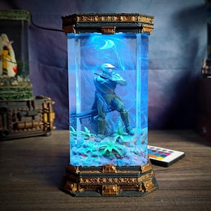 May include: A decorative light-up display featuring a soldier figure inside a clear, rectangular case. The figure is in a combat stance, surrounded by blue light and a swirling effect. The base and top have a gold and black trim.
