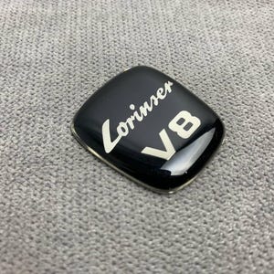 Puede incluir: Emblema Lorinser negro con letras blancas y un logotipo "V8" blanco.