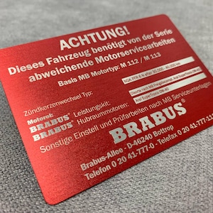 Puede incluir: Etiqueta de advertencia de metal rojo con texto blanco que dice: "ACHTUNG! Este vehículo requiere trabajos de servicio especiales de la serie. Tipo de motor MB básico: M 112/M 113. Tipo de reemplazo de bujías: Motorol: BRABUS Kit de rendimiento: NGK PFR 6 N después de 30.000-40.000 km. Tipo de aceite según las especificaciones de MB: Aral SuperTronic 0W-40. Otros ajustes e inspecciones de acuerdo con las pautas de servicio de MB. BRABUS. Brabus-Allee - D-46240 Bottrop. Teléfono 0 20 41-777-0 - Fax 0 20 41-777-111"