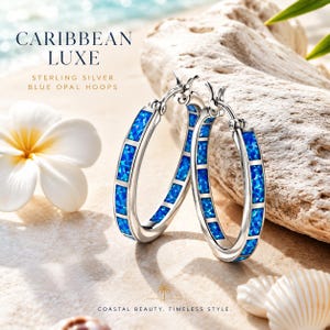 May include: Sterling silver hoop earrings with blue opal inlays. The earrings are displayed on a sandy surface with a white flower and seashells. The text reads "CARIBBEAN LUXE" and "COASTAL BEAUTY. TIMELESS STYLE."