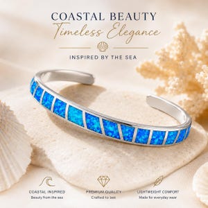 May include: A silver cuff bracelet with a rectangular blue opal inlay. The bracelet is displayed on a light-colored stone with seashells and coral in the background. The text reads "COASTAL BEAUTY, Timeless Elegance, INSPIRED BY THE SEA."