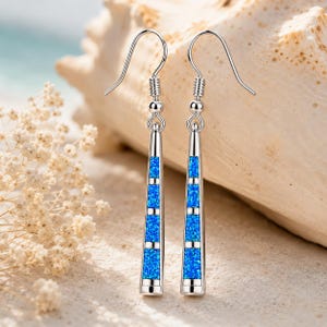 May include: A pair of silver dangle earrings with a rectangular design. The earrings feature a vibrant blue opal inlay with a linear pattern. The earrings are suspended from a silver hook.