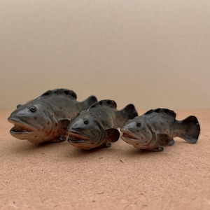 May include: Three ceramic fish figurines in various sizes. The fish are gray with black spots and red accents. The largest fish is on the left, the smallest is on the right.