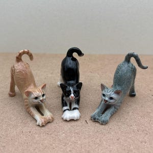 May include: Three ceramic cat figurines in a stretching pose. The cats are orange and white, black and white, and grey and white.