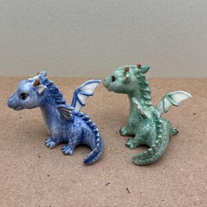 May include: Two small ceramic dragon figurines. One is blue with white wings and the other is green with white wings.