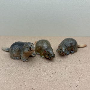 May include: Three small, grey and brown ceramic figurines of rodents. The figurines are posed in a sitting or lying position.
