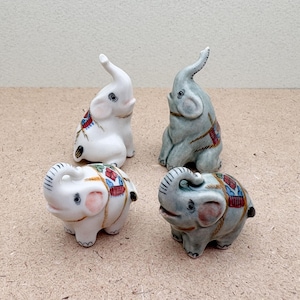 May include: Four ceramic elephant figurines, two white and two gray, with colorful painted details. The elephants are in various poses, with their trunks raised.