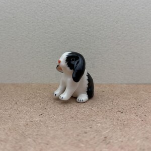 May include: A small ceramic figurine of a black and white rabbit sitting on a brown surface. The rabbit has a pink nose and black eyes.
