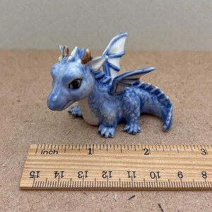 May include: A small blue and white ceramic dragon figurine with wings, measuring approximately 2 inches long. The dragon has a detailed face with gold accents.