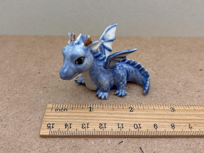 May include: A small blue and white ceramic dragon figurine with wings, measuring approximately 2 inches long. The dragon has a detailed face with gold accents.