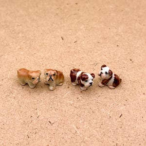 May include: Four miniature ceramic bulldog figurines. Two are brown and white, one is brown, and one is white with brown spots.