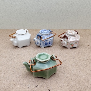 Peut inclure: Quatre petites théières en céramique avec des poignées dorées. Les théières sont de différentes couleurs et motifs, notamment blanc, bleu, vert et rose.
