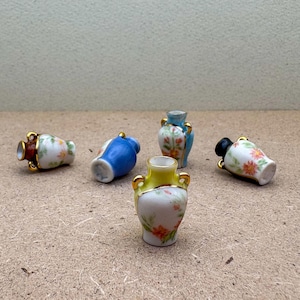 May include: Five miniature ceramic vases with floral patterns. The vases are in various colors, including blue, yellow, and white. They have gold accents and are arranged on a brown surface.