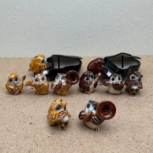 May include: A collection of ceramic owl figurines in various poses, some playing musical instruments like a trumpet, violin, and drums. Two black grand pianos are also present. The owls are primarily brown, yellow, and white.