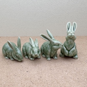 Puede incluir: Cuatro figuritas de conejo de cerámica en un esmalte verde. Los conejos están en varias poses, algunos sentados y otros tumbados.