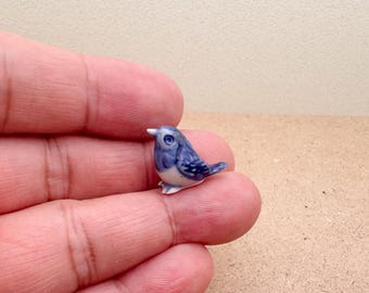 May include: A small, ceramic bird figurine. The bird is primarily blue with white accents on its belly and feet. It has a detailed design and is perched on a surface. The figurine is a decorative item.