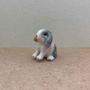 May include: A small ceramic figurine of a gray and white rabbit sitting with its ears perked up.