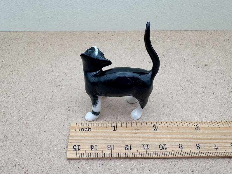 K&ouml;nnte beinhalten: Kleine Katze-Figur aus Keramik in Schwarz und Wei&szlig;. Die Katze steht mit erhobenem Schwanz und zur&uuml;ckgeneigtem Kopf. Die Figur ist etwa 5 cm lang.