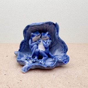 Peut inclure: Figurine en céramique représentant trois grenouilles bleues sur une feuille bleue. Les grenouilles, avec leurs ventres blancs, sont enlacées. La feuille est d'un bleu profond.