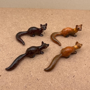 Peut inclure: Quatre figurines d'animaux en céramique miniature de belettes dans différentes poses. Les belettes sont peintes dans des tons de brun et de beige.