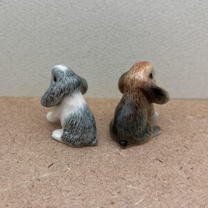May include: Two small ceramic rabbit figurines. The rabbit on the left is white with gray markings. The rabbit on the right is brown with gray markings.