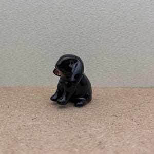 May include: A small black ceramic rabbit figurine with floppy ears. The rabbit is sitting with its head tilted to the side.