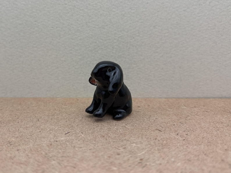 May include: A small black ceramic rabbit figurine with floppy ears. The rabbit is sitting with its head tilted to the side.