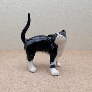 K&ouml;nnte beinhalten: Keramikfigur einer Katze im Tuxedo-Muster, mit gl&auml;nzendem Schwarz-Wei&szlig;-Finish. Die Katze steht mit nach oben geneigtem Kopf und gew&ouml;lbtem Schwanz. Die Pfoten der Katze sind wei&szlig;, die Nase rosa. Dekoration.