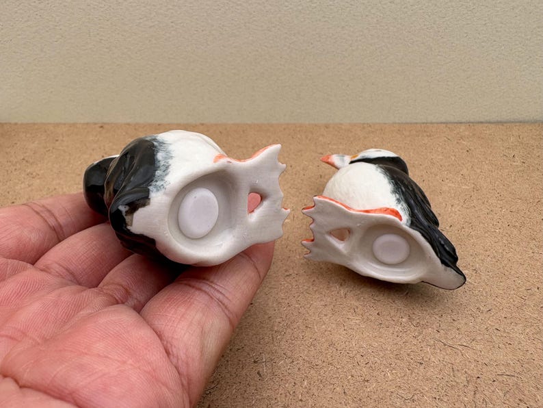 May include: Two ceramic salt and pepper shakers shaped like puffins. The puffins are black and white with orange beaks. The shakers are upside down, showing the white ceramic bottoms with a hole in the center.