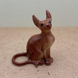 K&ouml;nnte beinhalten: Eine braune Keramikfigur eines Katers mit gro&szlig;en Ohren und einem langen Schwanz. Der Kater sitzt mit dem Kopf nach oben geneigt und offenen Augen.