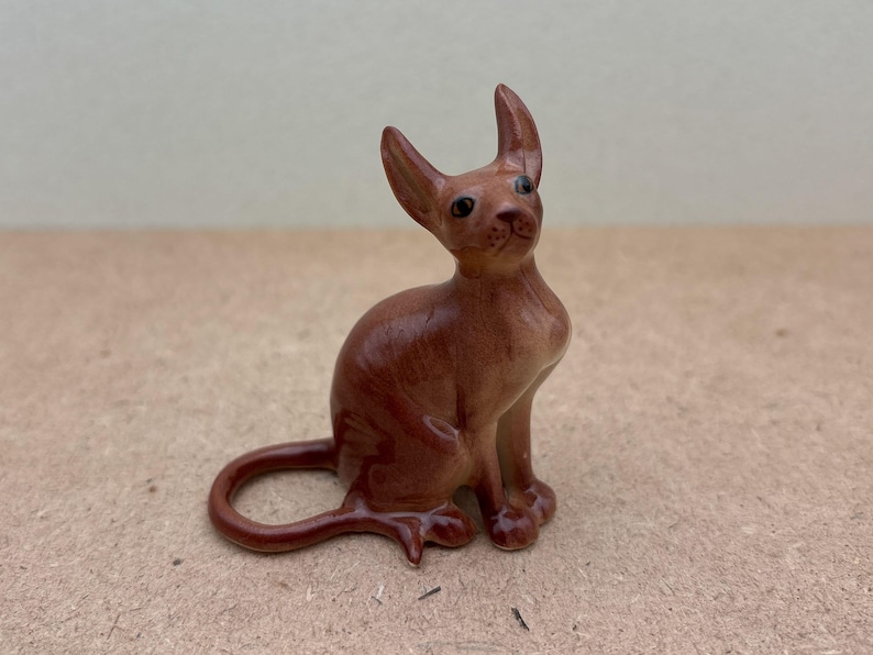 K&ouml;nnte beinhalten: Eine braune Keramikfigur eines Katers mit gro&szlig;en Ohren und einem langen Schwanz. Der Kater sitzt mit dem Kopf nach oben geneigt und offenen Augen.