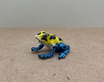 Handbeschilderd keramisch beeldje van een pijlgifkikker, blauw en geel amfibie decor, klein dierenbeeldje voor natuurliefhebbers en verzamelaars.
