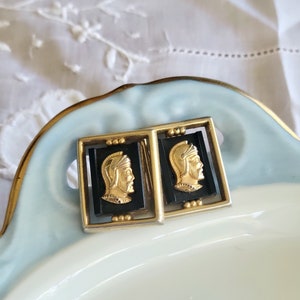May include: A pair of gold cufflinks with black enamel and a gold image of a man in a helmet.
