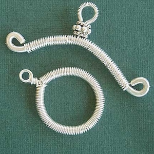 Può includere: Due pezzi di gioielleria in filo d'argento. Uno è un pezzo curvo con un perno d'argento in cima. L'altro è un pezzo rotondo.