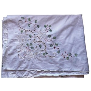 May include: White linen tablecloth with embroidered floral and vine design. The embroidery features openwork details, green leaves, and red accents. The tablecloth is folded, showing the scalloped edge.