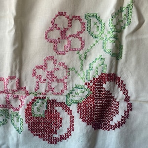 May include: White fabric with red and green embroidered flowers and cherries. The embroidery is done in a cross-stitch pattern.