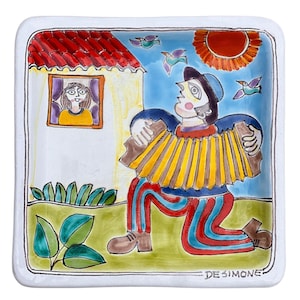 May include: Square ceramic plate with a whimsical illustration. A musician plays an accordion, wearing a blue hat and striped pants. A woman looks out a window. The plate has a red roof, blue sky, and the artist's signature.