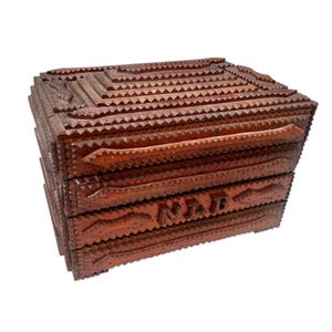 May include: A handcrafted wooden box with a dark brown finish. The box features intricate, carved geometric patterns and the word "NAD" carved into the front. The box has a rectangular shape with a hinged lid.
