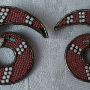 May include: A pair of earrings made of small red and white beads, with a clear rhinestone in the center of each earring. The earrings are shaped like a spiral.