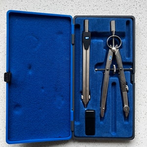 May include: A blue case with a compass and a ruler inside. The compass has a silver finish and a blue circle on the top. The ruler is also silver and has a blue circle on the top.